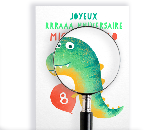 Une loupe posée sur une carte d'anniversaire personnalisée illustrée d'un dinosaure vert et d'un ballon rouge portant le chiffre 8, sur fond blanc.